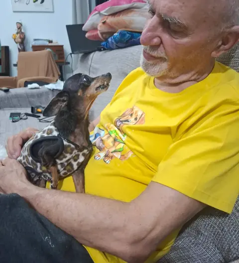 Benedito Furtado acolhe um cão pequeno no colo.